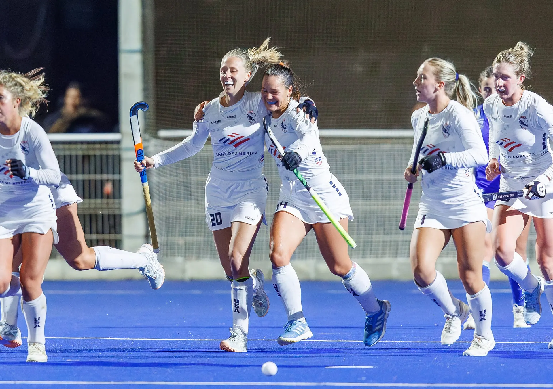 U.S. women's field hockey players celebrate a goal together on a blue pitch.
