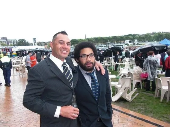 Rodney Taylor and Tatafu Polota-Nau smile together in suits at an outdoor event.