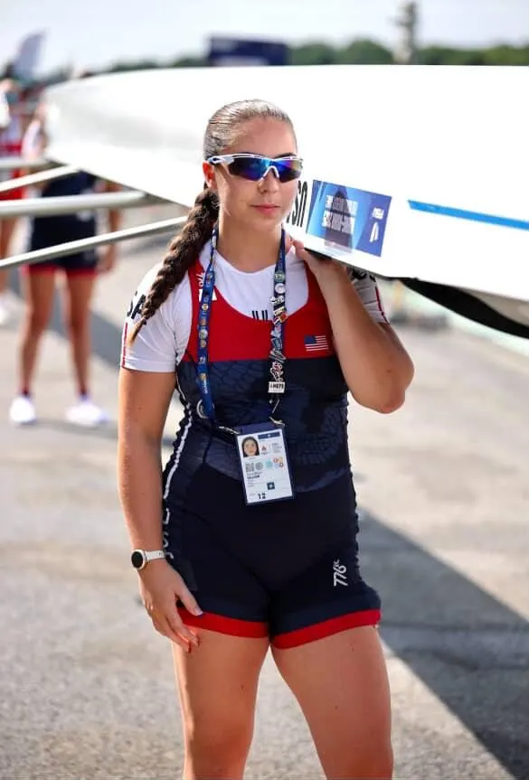 Midori Galligan carries a rowing shell's oar over her shoulder in team kit.